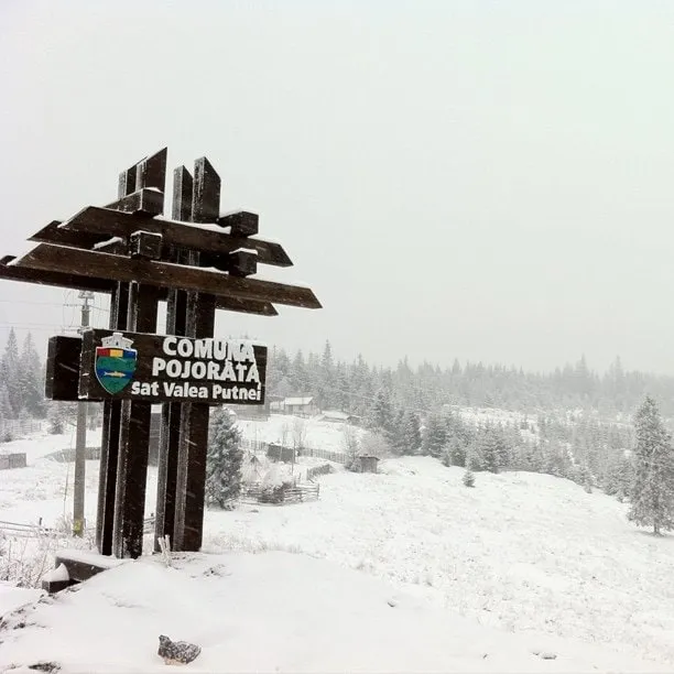 Wooden sign for the commune of Pojorâta, Valea Putnei village, against a snowy landscape