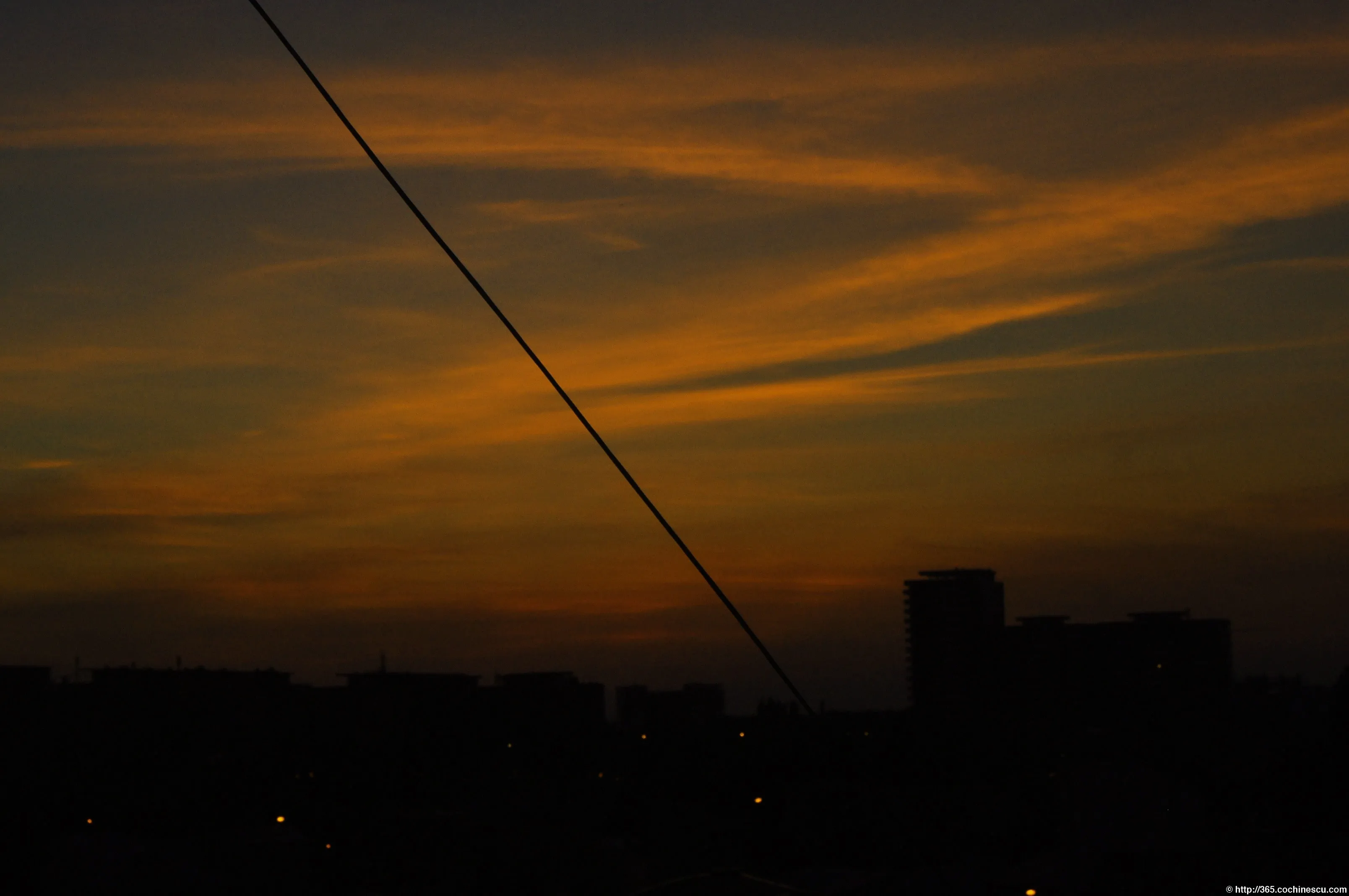 Orange clouds stretch over the dark city skyline at sunset.