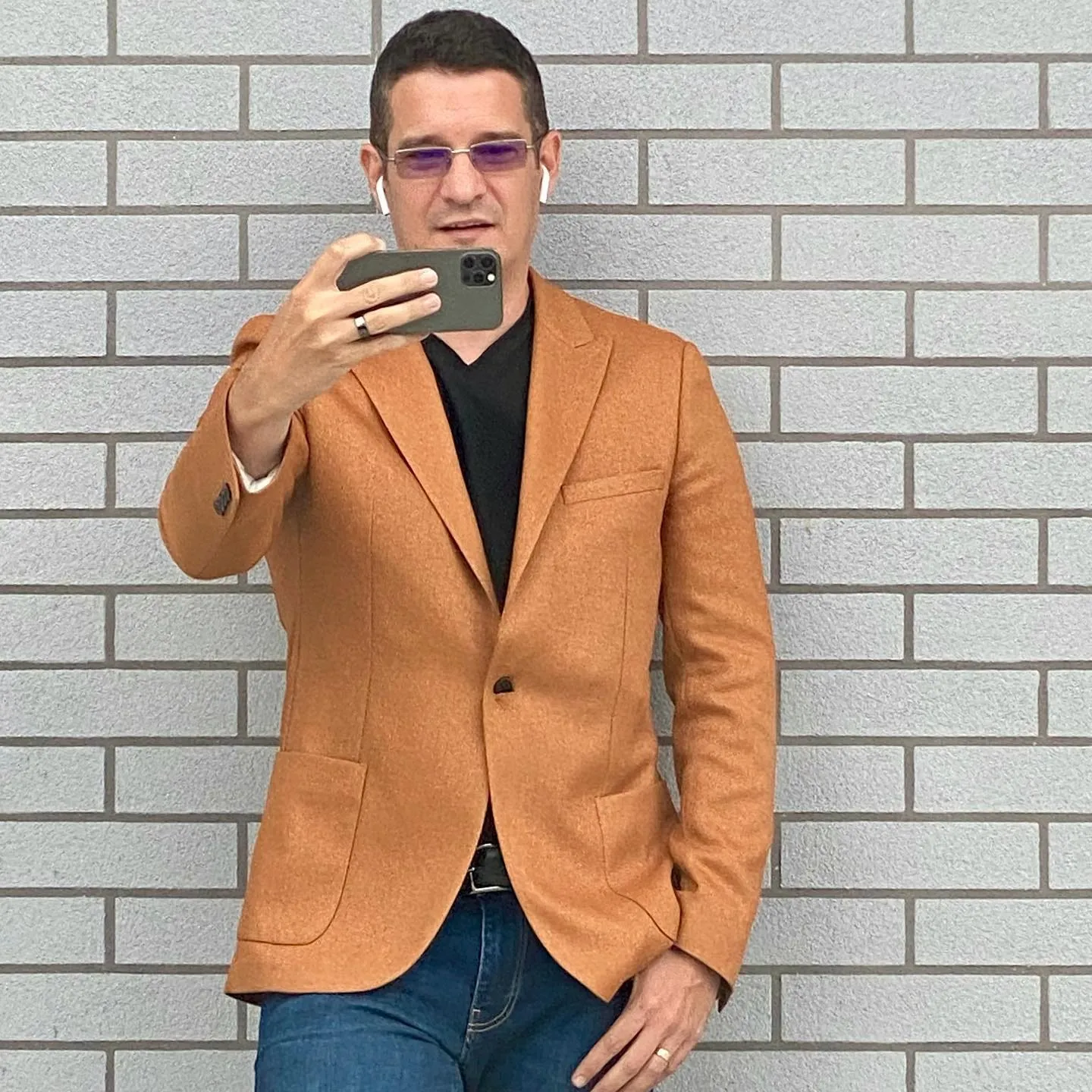 Sebastian Cochinescu takes a mirror selfie in a brown jacket against a gray brick wall.
