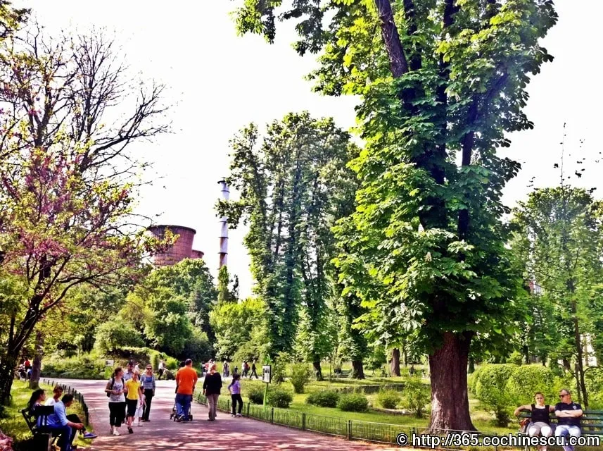 Visitors stroll through the botanical garden, with old industrial buildings in the background.