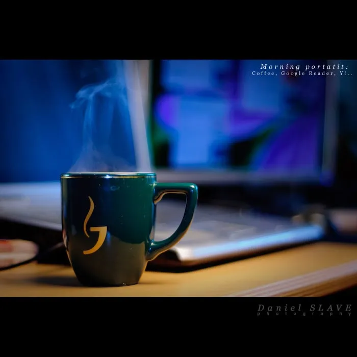 A steaming cup of coffee sits on the desk, in front of a laptop.