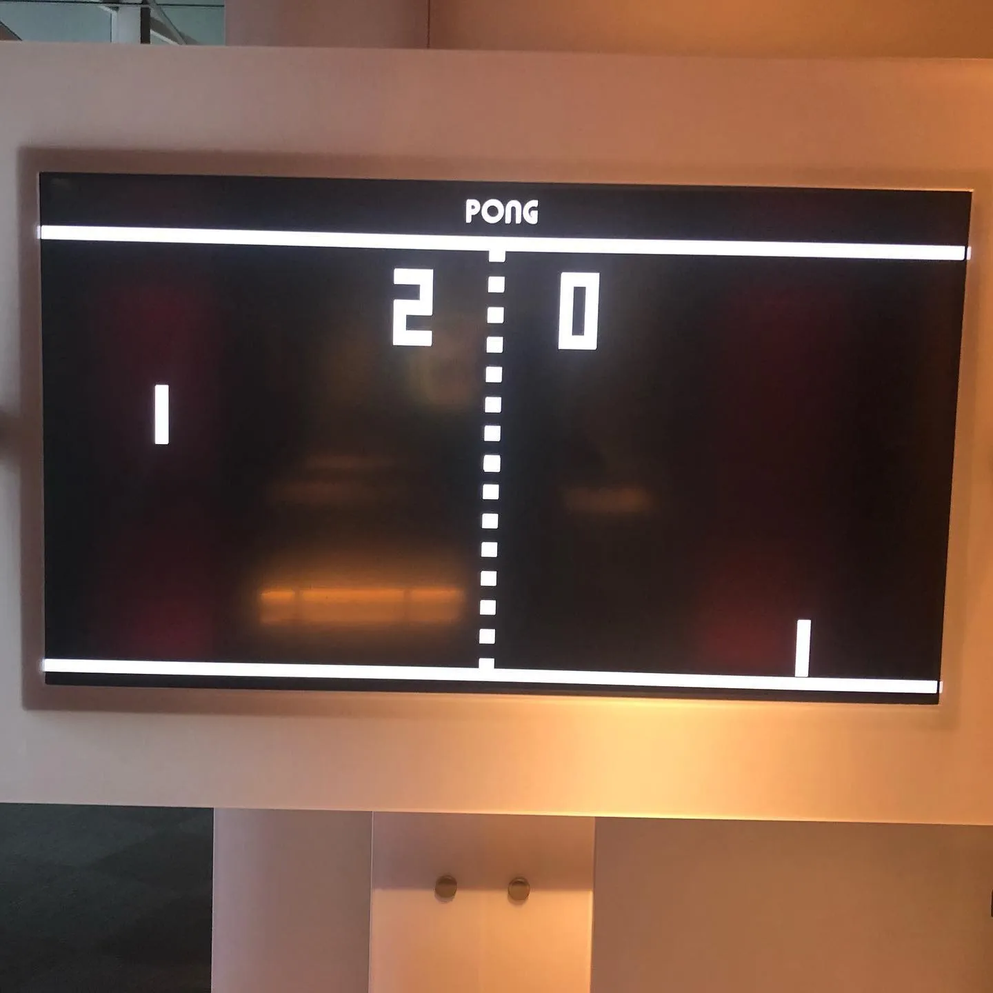 A wall-mounted screen shows a classic Pong game with the score 2 to 0.