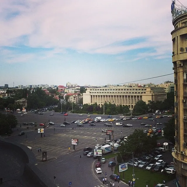 Aerial view of Victory Square in Bucharest, with the central parking lot empty, traffic on the roundabout and government buildings in the background.