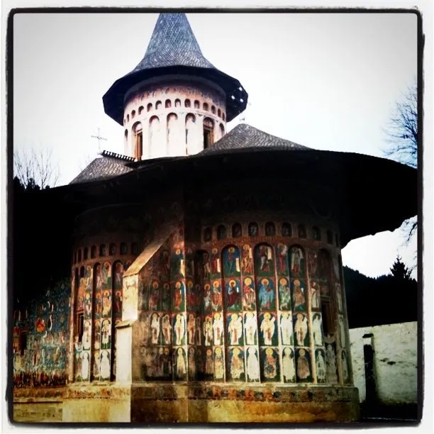 The exterior of the church at Voroneț Monastery, covered in colorful frescoes beneath a dark roof