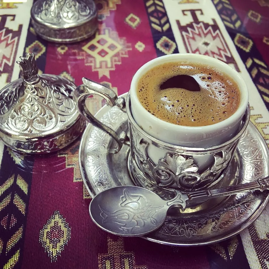Traditional coffee in an ornate silver cup holder with a spoon on a patterned tablecloth.