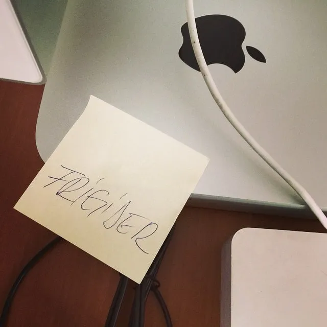Yellow sticky note with the word Fridge stuck to the back of a silver iMac with the Apple logo