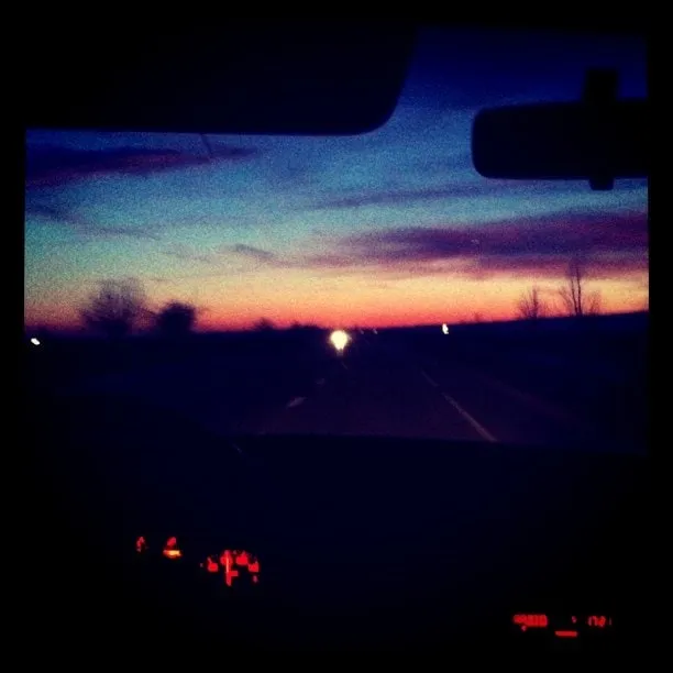 View from inside a car of a highway at dusk with the low sun on the horizon