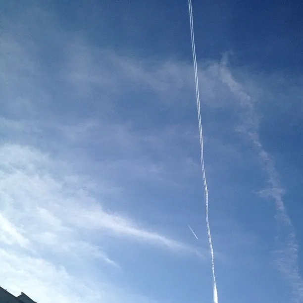 A plane leaves a vertical white trail across a blue sky with wispy clouds.