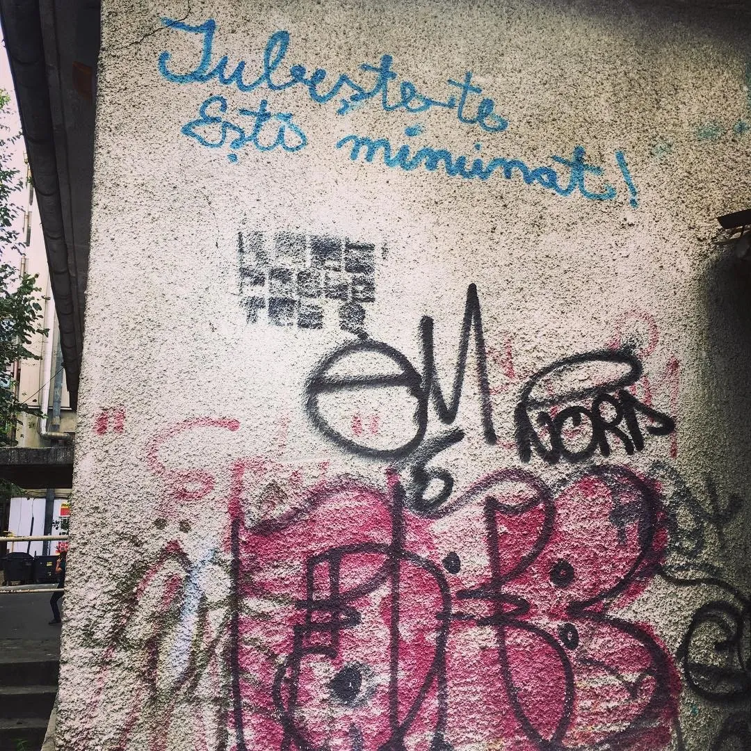 Concrete wall with blue handwritten text reading Iubeste-te esti minunat above pink and black graffiti.