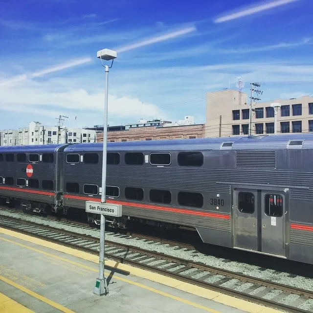 A double-decker Caltrain train at the platform in San Francisco, under a blue, cloudy sky.