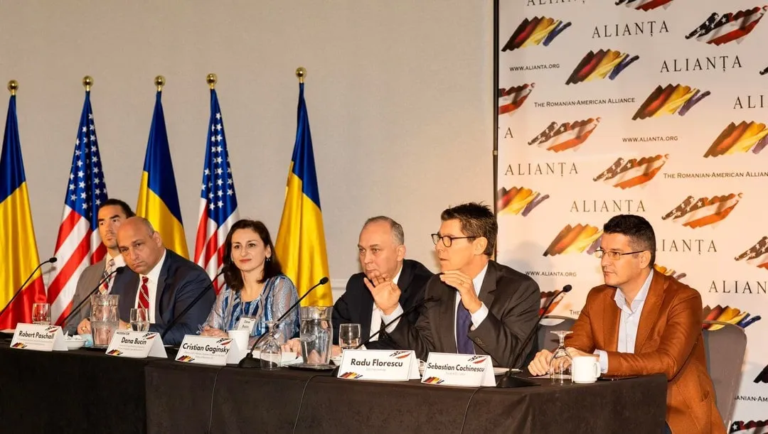 Panelists including Sebastian Cochinescu sit at a conference table with microphones under Romanian and US flags at an Alianța event.