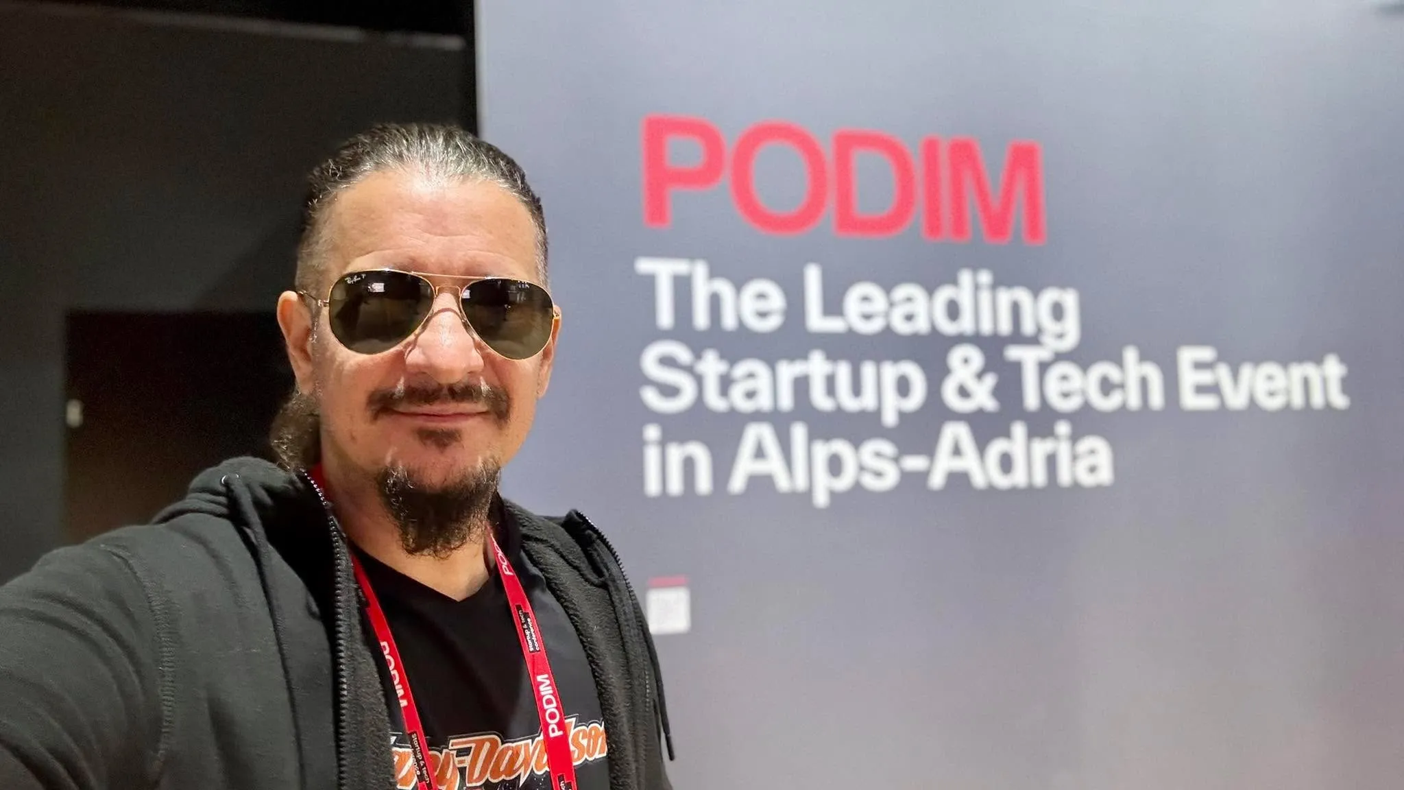 Sebastian Cochinescu takes a selfie in front of a Podim startup and technology event sign.