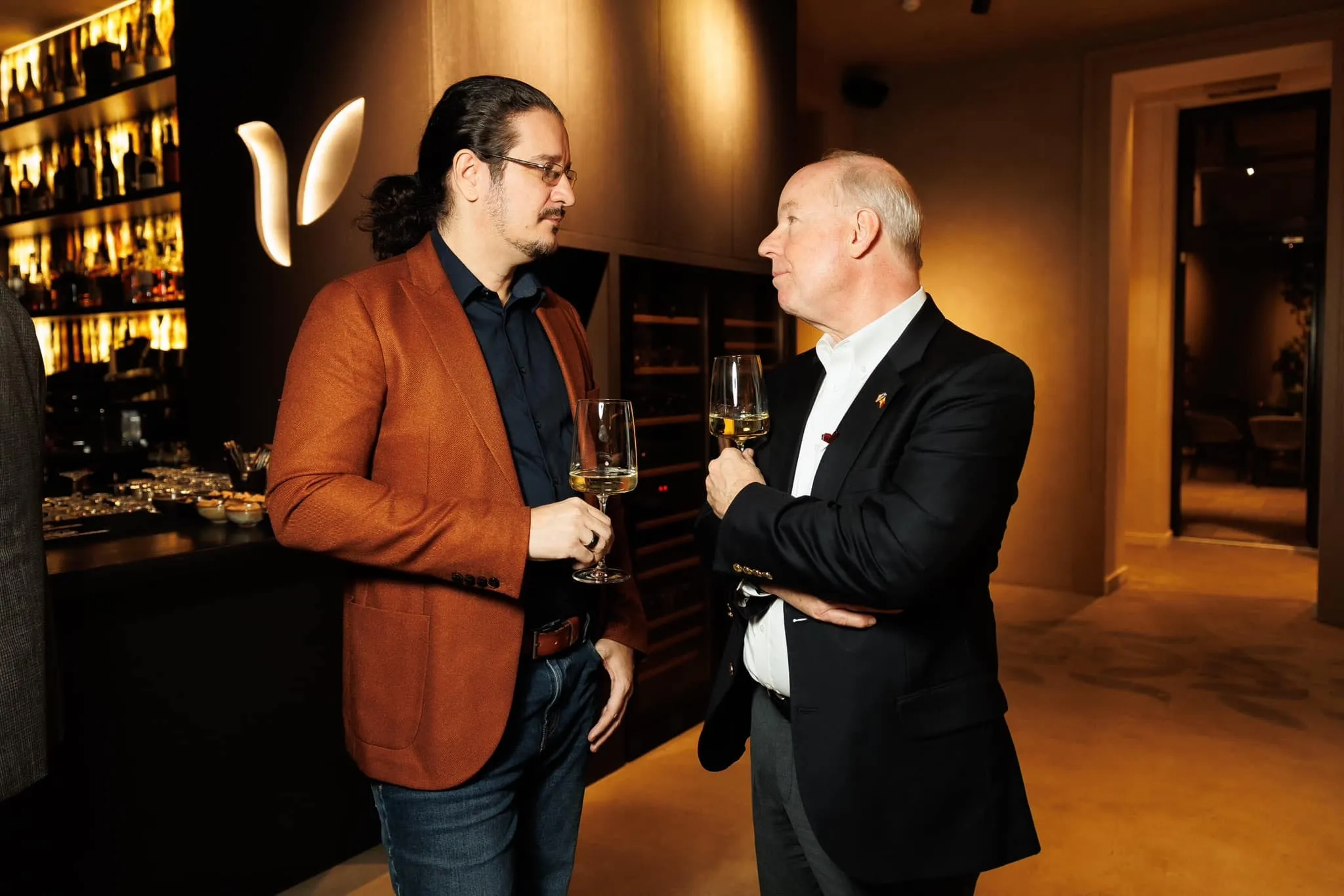 Sebastian Cochinescu and U.S. Ambassador Kent D. Logsdon converse while holding wine glasses in a lounge.
