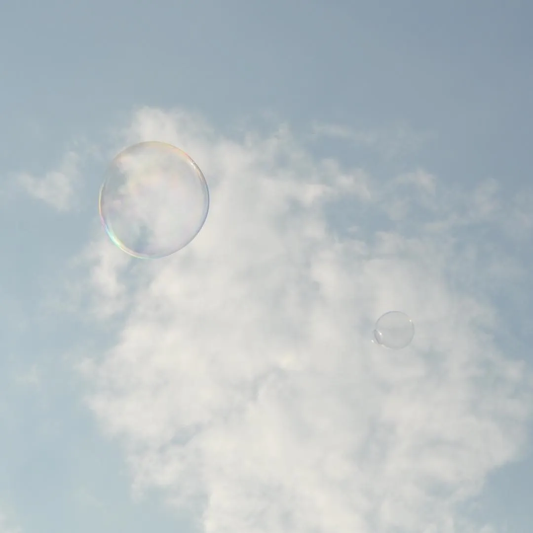 Iridescent soap bubbles floating against a pale blue sky with white clouds