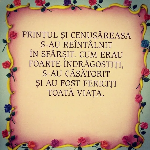Un tort roz, cu o bordură din panglică galbenă și trandafirași, pe care este scris textul în limba română că prințul și Cenușăreasa se căsătoresc.