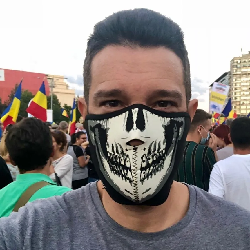 Sebastian Cochinescu wears a skull-patterned mask at a crowded protest with Romanian flags.
