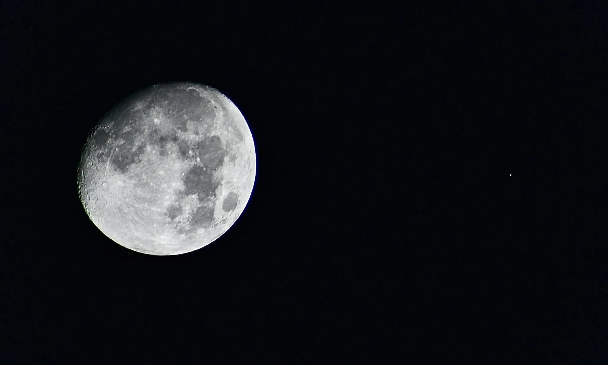 A nearly full moon and a small bright point of light, Mars, against a black night sky.