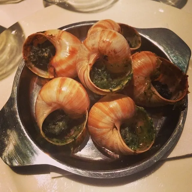 Metal pan of escargot shells filled with green herb butter on a white tablecloth.