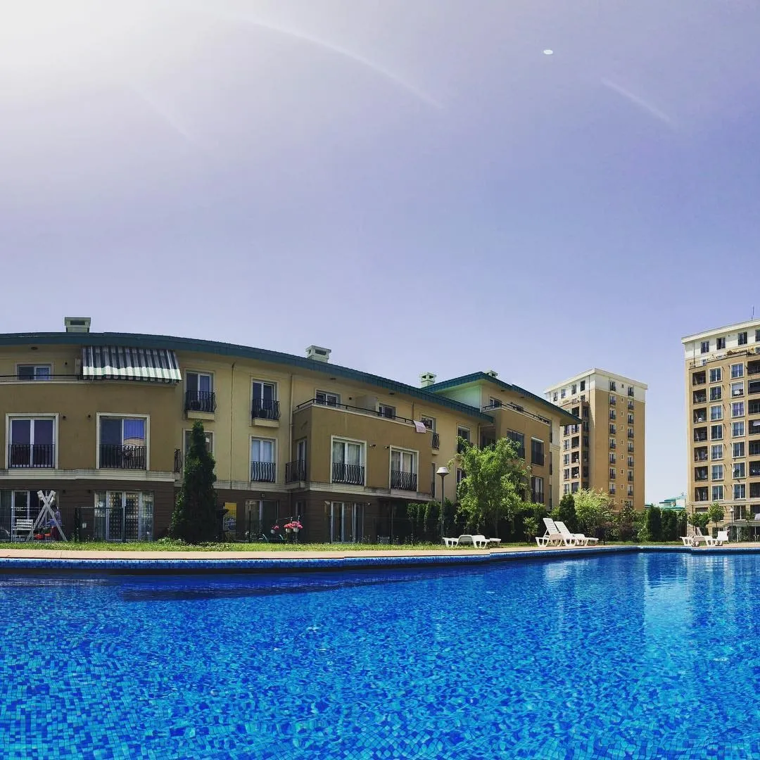 Blue outdoor swimming pool in front of beige Cosmopolis residential buildings under a bright sky