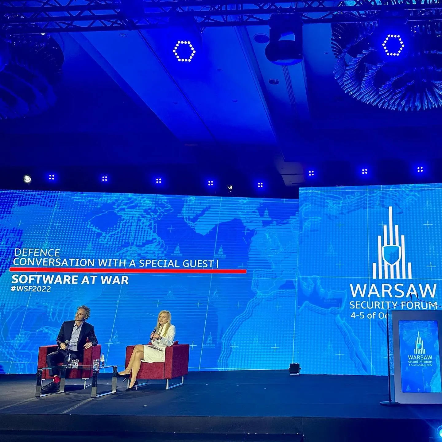 Alex Karp and a moderator sit on stage at the Warsaw Security Forum under a Software at War screen.
