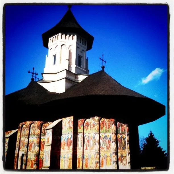 The white tower and fresco-covered façade of Moldovița Monastery against a blue sky.