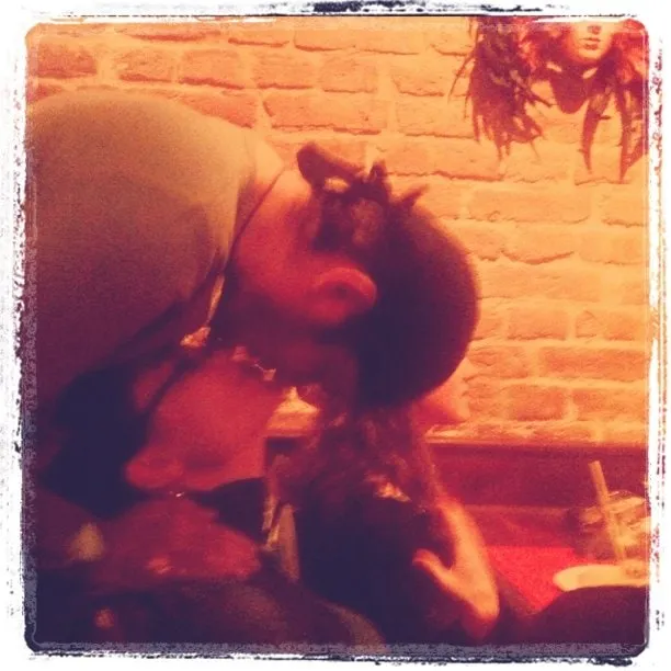 A man and a girl hug indoors, in warm light, against a brick wall.