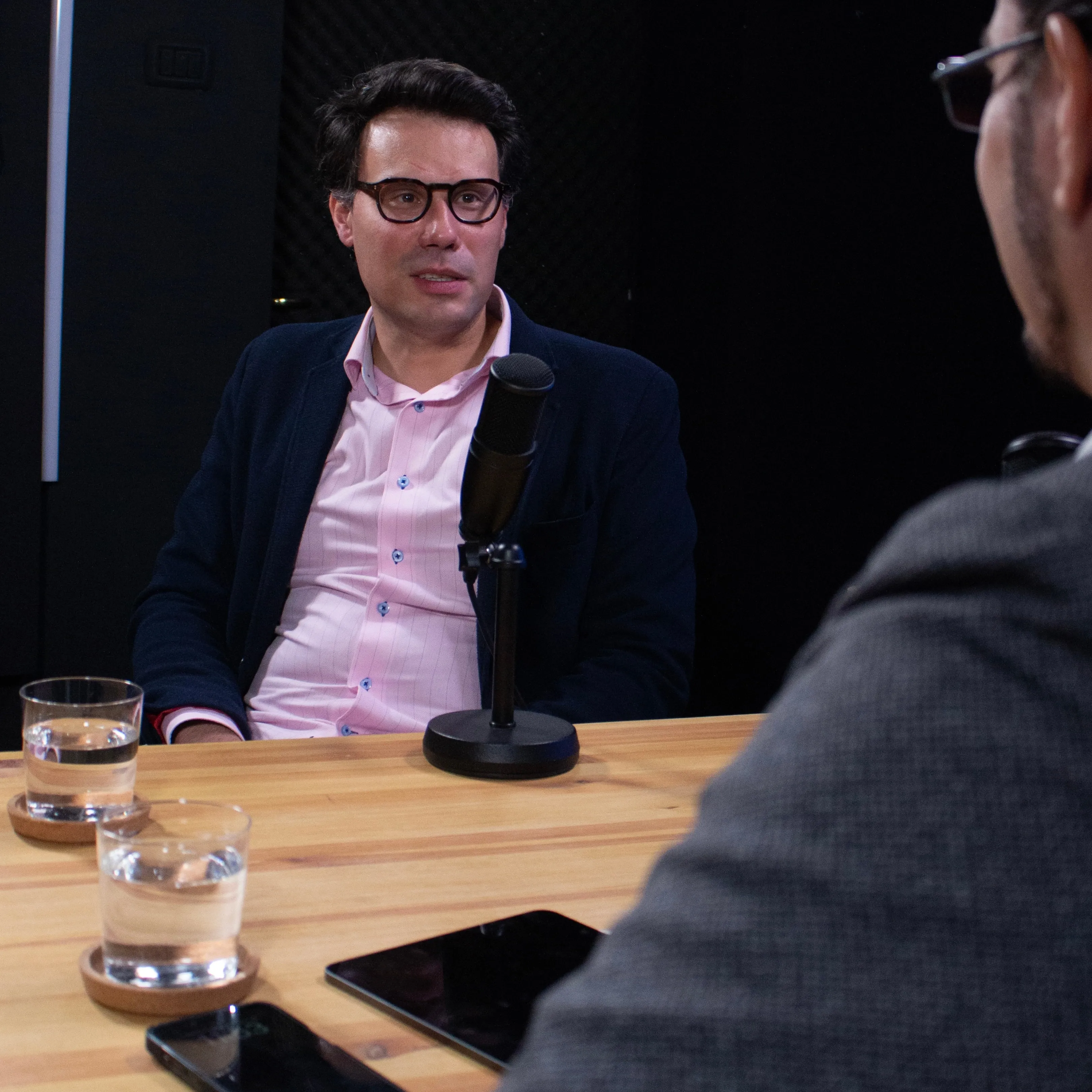 A guest speaking into a microphone at a podcast table