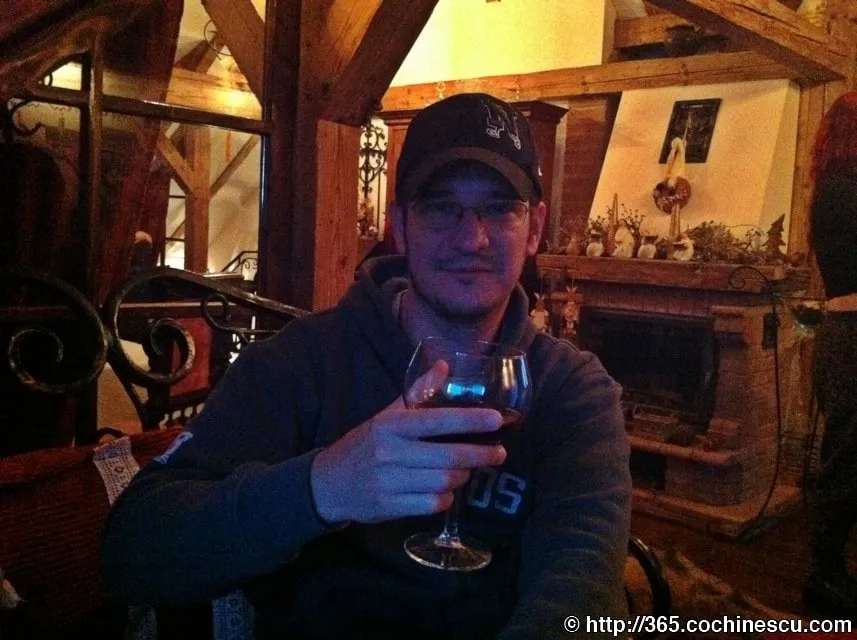 A man sitting in a rustic room holds a glass of wine in his hand.
