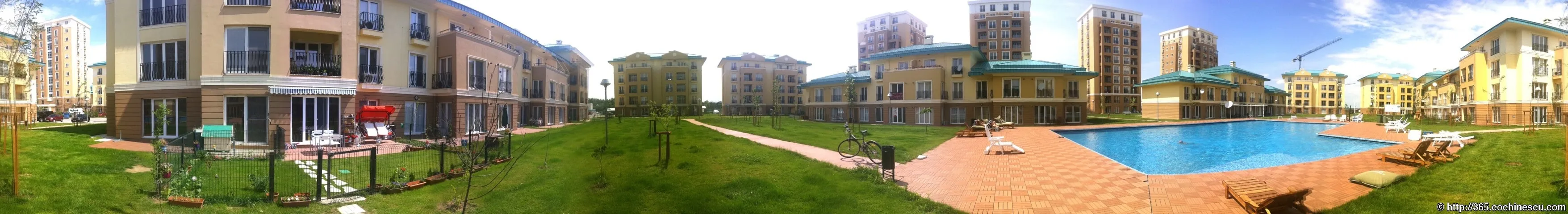A wide panorama shows the swimming pool, green spaces, and apartment buildings of the Cosmopolis complex.