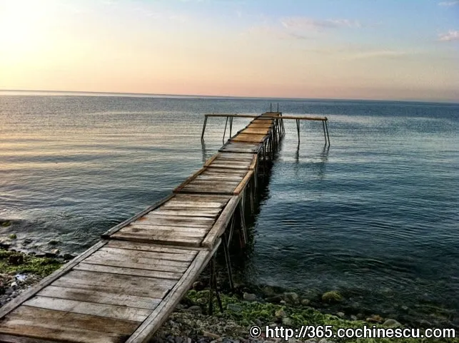 An old wooden pier juts out over the calm water beneath a pastel sky.